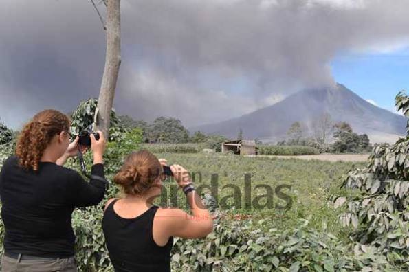 Turis asing menjepret kamera saat mengabadikan Gunung Sinabung yang menyemburkan awan panas sekira 2 Km ke arah tenggara, Rabu (24/ 9). (Andalas)